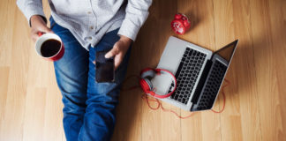 Individual sitting on their laminate floor drinking coffee and using their phone