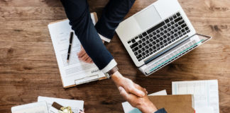 Two individuals shaking hands across a work table