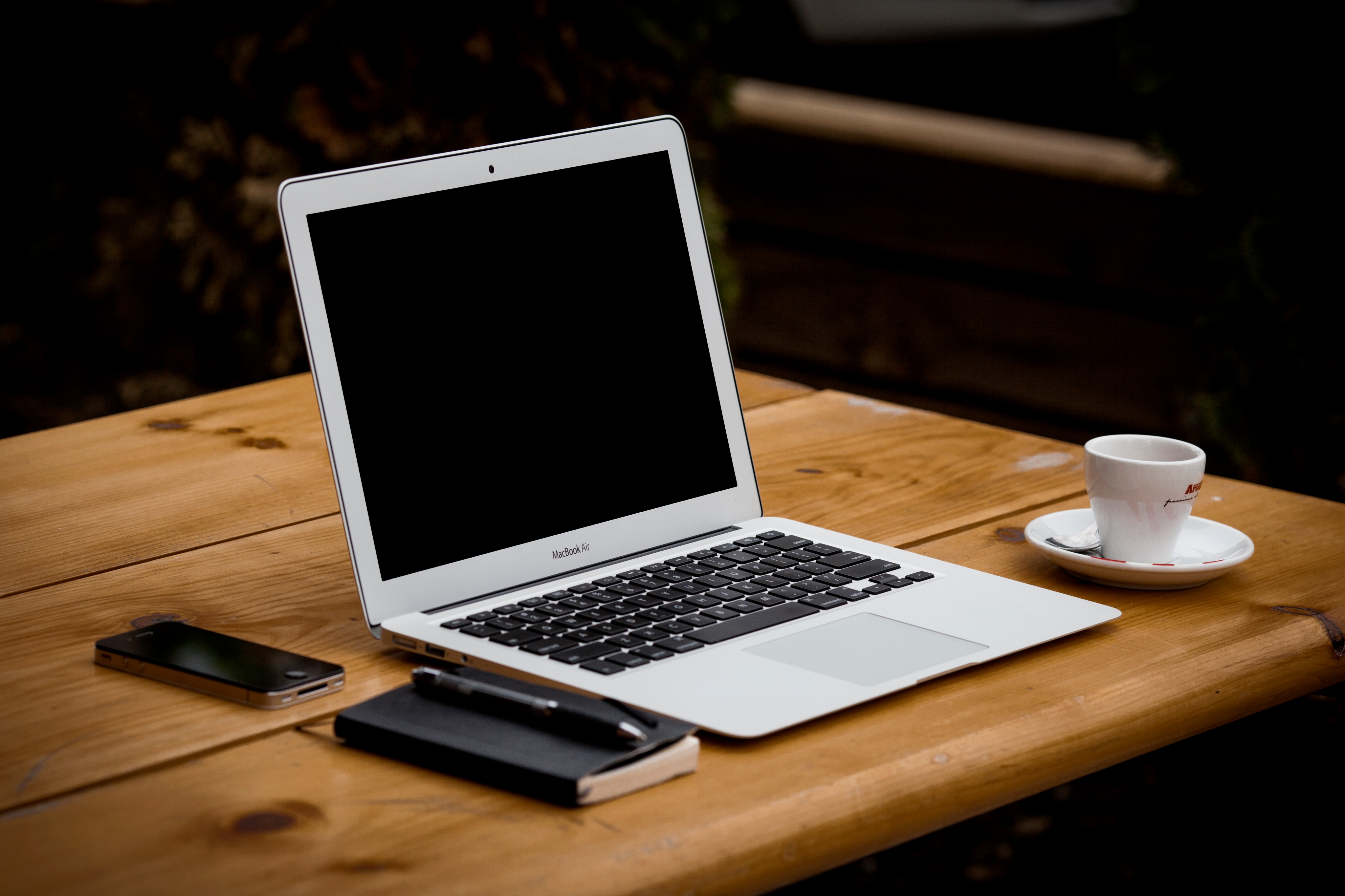 A laptop, a notebook, a phone, and a coffee cup atop a wooden table