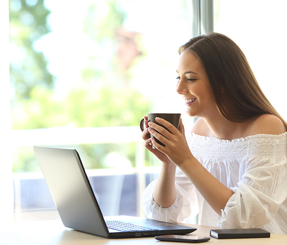 An individual drinking coffee at their laptop